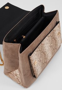 Bolso de hombro de ante color marrón claro con un panel texturizado de piel de serpiente. Presenta un cierre a presión dorado y un interior de tela negra con bolsillos con cremallera.