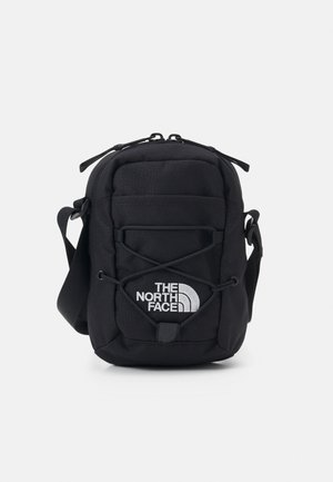 Compact zwart schoudertasje met vooraan elastisch bungee-koord en wit "The North Face" logo op het voorvak.