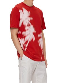 T-shirt en coton rouge avec impression de palmier blanc, col rond, manches courtes et coupe décontractée, associé à un short de couleur claire.