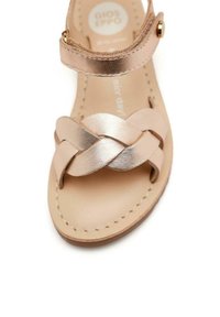 Sandalo in elegante rosa dorato metallico con cinturini in pelle intrecciata, cinturino alla caviglia e soletta liscia color beige. Design open-toe su una suola piatta.