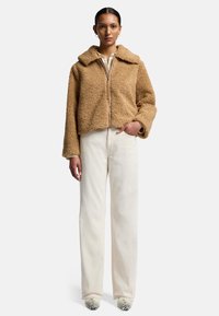 Brun faux fur-jacka med krage, dragkedja och boxig passform, tillsammans med off-white vida byxor och mönstrade skor.