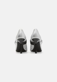 Pantofi cu toc înalt argintii, cu vârful ascuțit, curea neagră și toc stiletto. Tocul este elegant și lucios pentru un contrast.