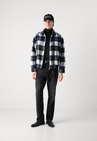 Plaid jacket in black, blue, and white; black turtleneck; black jeans; black shoes; black cap with "BOSS" logo.