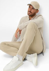 Beige pet, crèmekleurige geribde trui, kaki broek en witte sneakers. De outfit heeft een casual ontwerp met een losse pasvorm en zachte texturen.