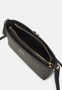 Malá crossbody taška s tmavě hnědým vzorovaným plátnem na vnějšku, černým podšívkou, zlatým zipem a nastavitelným popruhem. Uvnitř se nachází jedna hlavní přihrádka.