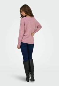 Pull en maille rose avec une coupe ample, doté de manches longues et d'un ourlet arrondi. Associé à un jean bleu foncé et des bottes noires à hauteur de genoux.