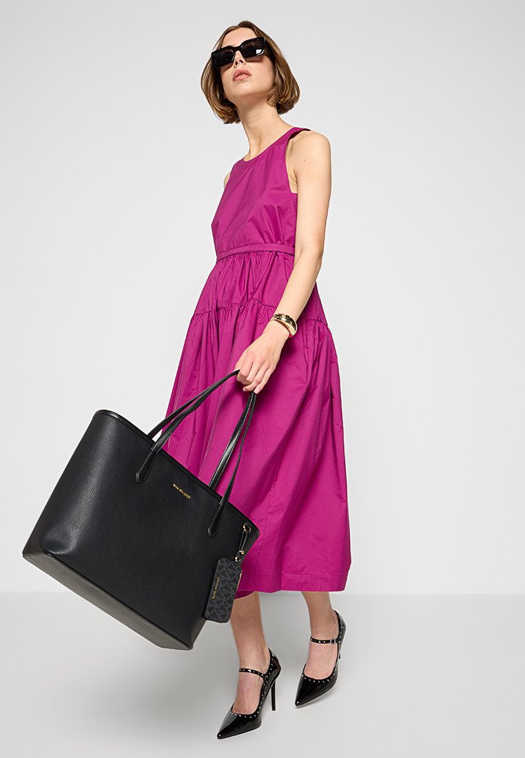 Fuchsia mouwloze jurk met een geplooide taille, gecombineerd met een zwarte leren tote bag en zwarte puntige hakken. Vloeiende textuur en minimale accenten.