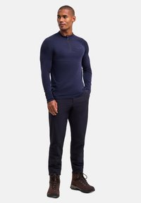 Marineblaues Langarmshirt mit halbem Reißverschluss, strukturierten Schulterakzenten, kombiniert mit schwarzer Hose und braunen Wanderschuhen.