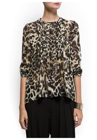 Blouse en satin avec un imprimé animal crème et marron, détails plissés à l'avant et manches trois-quarts, associée à un pantalon noir.