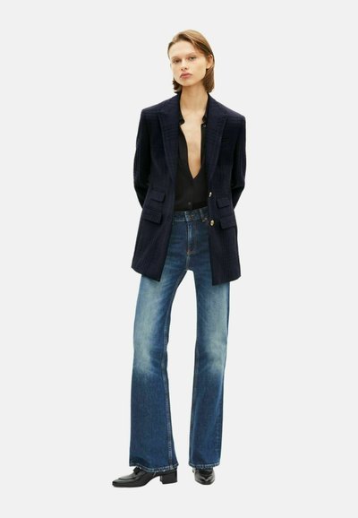 Marineblazer aus strukturiertem Stoff, mit Vordertaschen und goldenen Knöpfen, kombiniert mit hellblauen ausgestellten Jeans und schwarzen Stiefeletten.