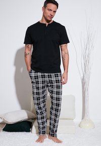 Maglietta henley nera a maniche corte abbinata a pantaloni da pigiama a scacchi in bianco e nero. Tessuto morbido, vestibilità rilassata, design semplice e bottoni visibili.