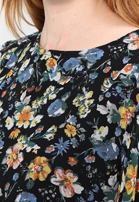 Květinová halenka s vícebarevnými květinami na černém pozadí, s kulatým výstřihem a krátkými rukávy, z lehké látky.