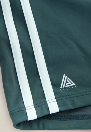 Ciemnozielone sportowe szorty z białymi paskami po bokach. Posiadają nadrukowane logo z geometrycznym wzorem. Gładki materiał odprowadzający wilgoć.