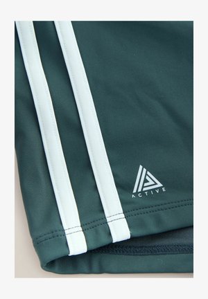 Sötétzöld atlétikai rövidnadrágok fehér oldalsávokkal. Geometriai mintás nyomott logóval. Simább, nedvességelvezető anyagból.