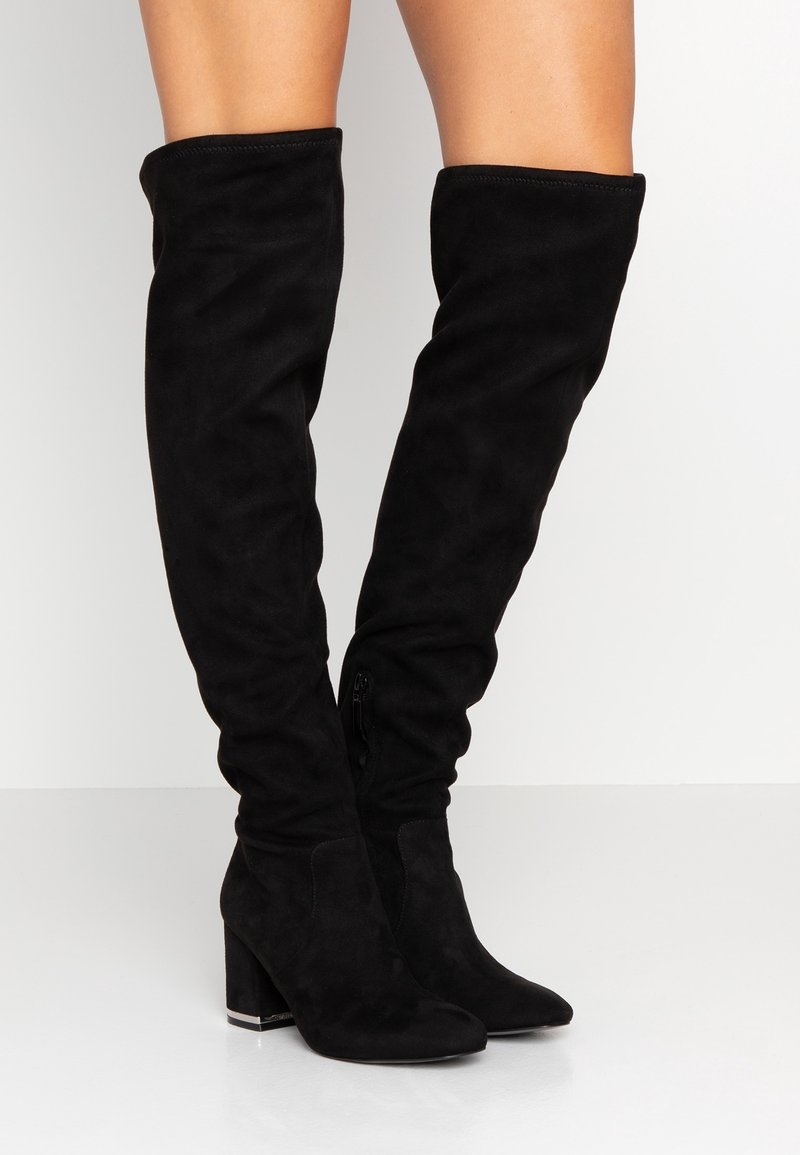 Bottes noires au-dessus du genou en daim, dotées d'un bout pointu, d'un talon bloc et d'une fermeture éclair latérale, avec une texture lisse et un design ajusté.