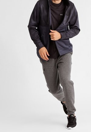 Šedé tepláky v kombinaci s tmavým tričkem s dlouhým rukávem a námořnickou mikinou na zip s texturovaným vzorem, vyzařující atletický styl.