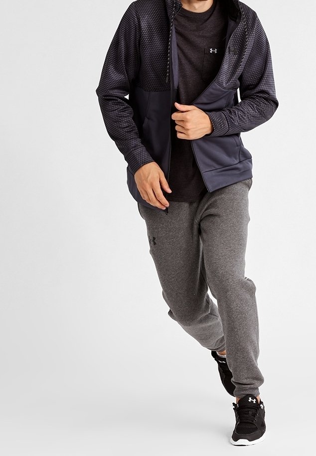 Pantaloni grigi abbinati a una maglietta a maniche lunghe scura e a una giacca con zip blu navy caratterizzata da un motivo testurizzato, che esprime uno stile atletico.