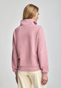 Ljusrosa sweatshirt med hög krage och ribbade muddar. Tillverkad av mjukt tyg, med avslappnad passform och cropped längd.