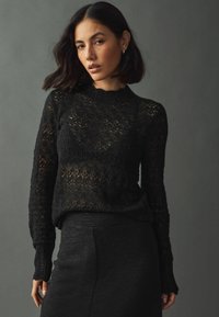 Maglione nero lavorato a maglia con motivo simile a pizzo, dotato di maniche lunghe e collo rotondo a costine. Tessuto testurizzato che completa una silhouette aderente.