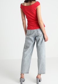 Red off-the-shoulder top with ruched design, paired with light blue high-waisted jeans. Black and white striped platform shoes.