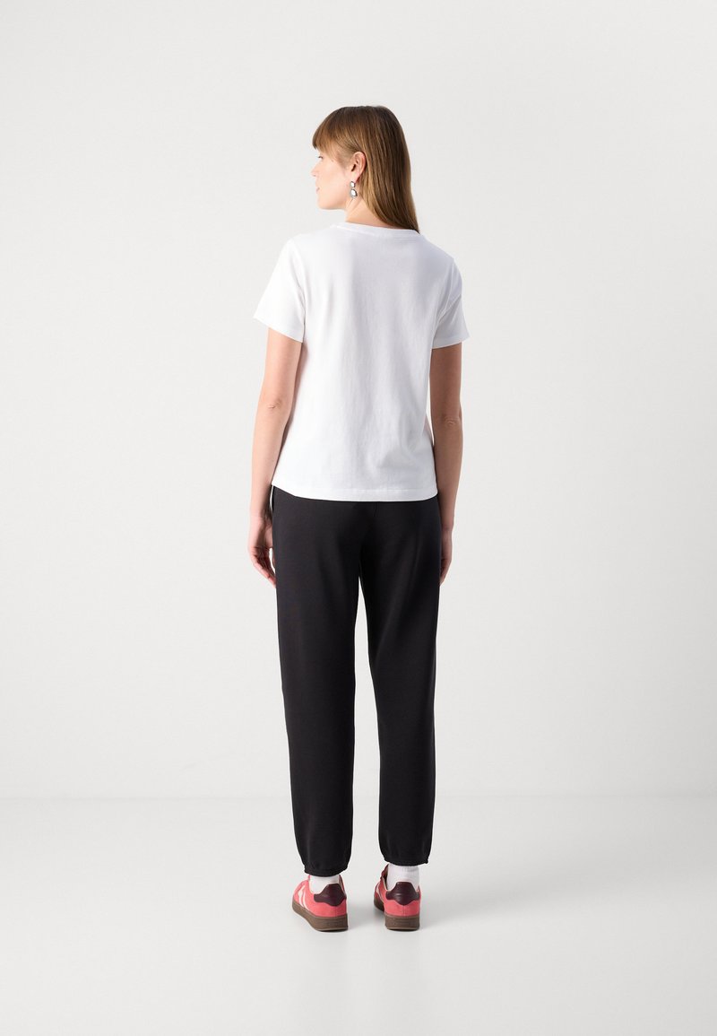 Weißes T-Shirt mit kurzen Ärmeln, kombiniert mit schwarzen Hosen, locker sitzend und ergänzt durch rote und rosa Sneaker sowie weiße Socken.