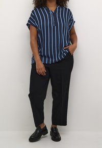 Chemise bleu marine à manches courtes avec des rayures verticales bleu clair, dotée d'une patte de boutonnage partielle. Portée avec un pantalon noir et des chaussures noires.