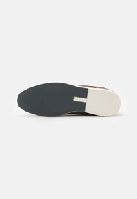 La suela del zapato presenta una superficie de goma texturizada de color gris oscuro con un perfil amplio y plano, y un borde blanco contrastante a lo largo del talón.
