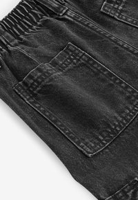 Pantaloni in denim nero con vita elasticizzata, dotati di molteplici tasche e una finitura testurizzata. Il tessuto presenta un leggero motivo sbiadito.