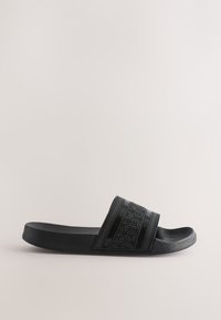 Ciabatta nera in gomma con cinturino testurizzato con motivi geometrici e strisce verticali, suola piatta con una leggera curvatura.