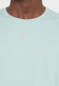 Jasnoniebieska sportowa koszulka z teksturowanej tkaniny, z delikatnym wytłoczonym logo na piersi i okrągłym dekoltem.