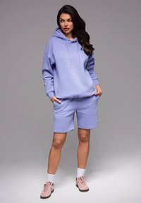 Hoodie lilas clair avec cordons, assorti à un short lilas clair. Avec une texture douce et un petit logo sur le short.