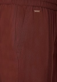 Närbild av en rostfärgad byxficka med elastisk midja och synliga sömdetaljer.