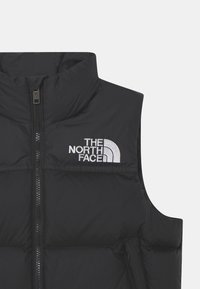 Svart isolerad väst med hög krage, dragkedja framtill och quiltat mönster. Har "The North Face"-logotyp i vitt på övre vänstra sidan.