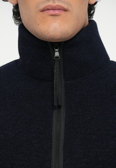 Dunkelblaue Fleecejacke mit hohem Kragen, Frontreißverschluss mit kontrastierendem Ziehband und strukturiertem Stoff.