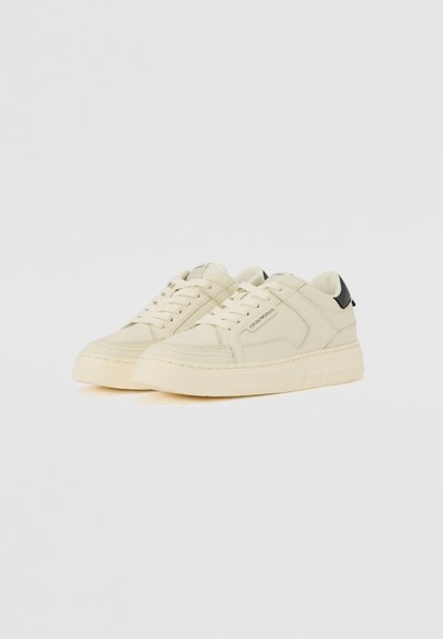 Nude sneakers with a leather upper, round toe, flat laces, textured panels, and a contrasting black heel accent. Thick rubber sole.