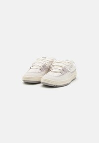Para białych i jasnoszarych sneakersów Nike z sznurówkami, teksturowanymi podeszwami i logo marki na jednolitym białym tle.
