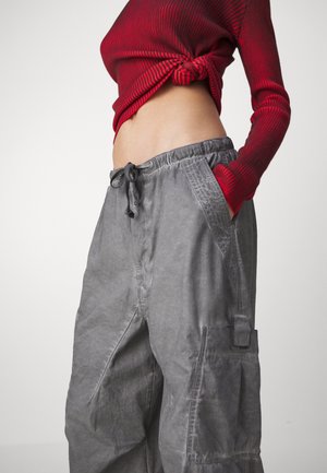 Šedé pracovní kalhoty s elastickým pasem, šňůrkou a bočními kapsami; textura látky s jemnými záhyby a volným střihem.