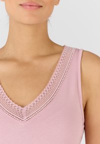 Top rosa con scollatura a V decorata con un delicato bordo in pizzo lungo il margine, che mette in risalto una texture di tessuto liscia e morbida.