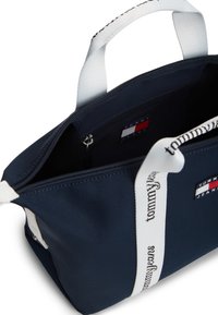 Τσάντα ώμου από ύφασμα σε ναυτικό μπλε με λευκές λαβές και λογότυπο. Το εσωτερικό διαθέτει τσέπες και κλείνει με φερμουάρ στην κορυφή για ασφαλή αποθήκευση.