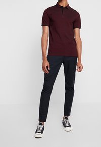 Polo bordeaux avec col et accents noirs, associé à un pantalon slim bleu marine et des baskets noires à semelles blanches.