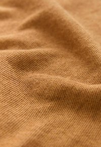 Gros plan d’un tissu doux et texturé couleur camel avec de fines côtes diagonales et des plis doux.