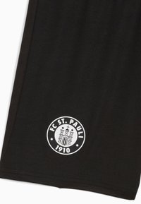 Svarta fotbollsshorts av tyg med en rund vit logotyp som har "FC ST. PAULI" och "1910" vid fållen. Slät textur, enkel design.