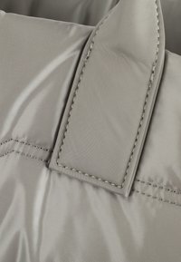 Tessuto in nylon grigio con una superficie liscia e cuciture visibili. Presenta una linguetta rettangolare con un'accortezza cucita, evidenziando la durabilità.