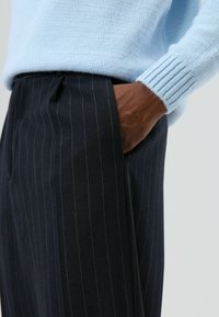 Marineblauwe krijtstreepbroek met een getailleerde pasvorm, gemaakt van een gestructureerde stof, voorzien van een zijzak en een subtiele plooi.