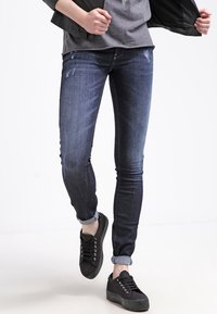 Jeans skinny in denim blu scuro con dettagli strappati, con risvolti, abbinati a sneaker in tela nera, con lacci rotondi e suole in gomma.