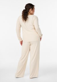 Hellbeiges, geripptes Langarmoberteil mit rundem Ausschnitt, kombiniert mit passenden, weit geschnittenen Hosen aus weichem Stoff, geeignet als Loungewear.