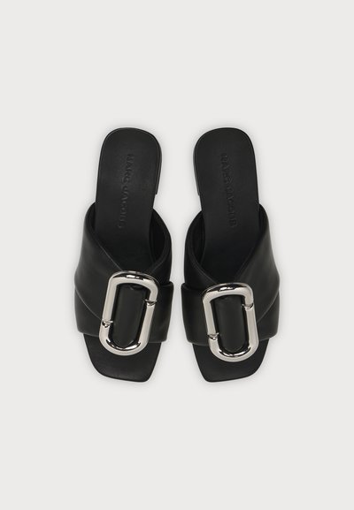 Paire de sandales noires à enfiler avec des larges brides et de grandes boucles ovales argentées, design plat à bout carré, vue de dessus.