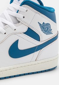 Basket Air Jordan montante blanc et bleu montrant les lacets, le swoosh Nike, le logo ailes Air Jordan et une semelle texturée en gros plan.