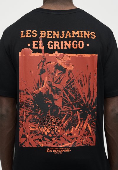Άτομο που φοράει σωμαρέρο και κρατάει τουφέκι, σκυμμένο σε ψηλό χορτάρι με μεγάλο φυτό αγαύης· κείμενο που γράφει "Les Benjamins El Gringo".