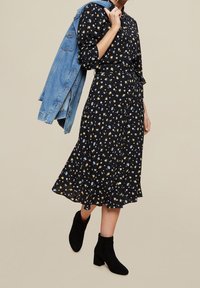 Abito midi floreale in tessuto nero, dotato di vita cincherata, maniche lunghe e orlo a strati. Abbinato a un giubbotto di denim chiaro e stivali neri alla caviglia.